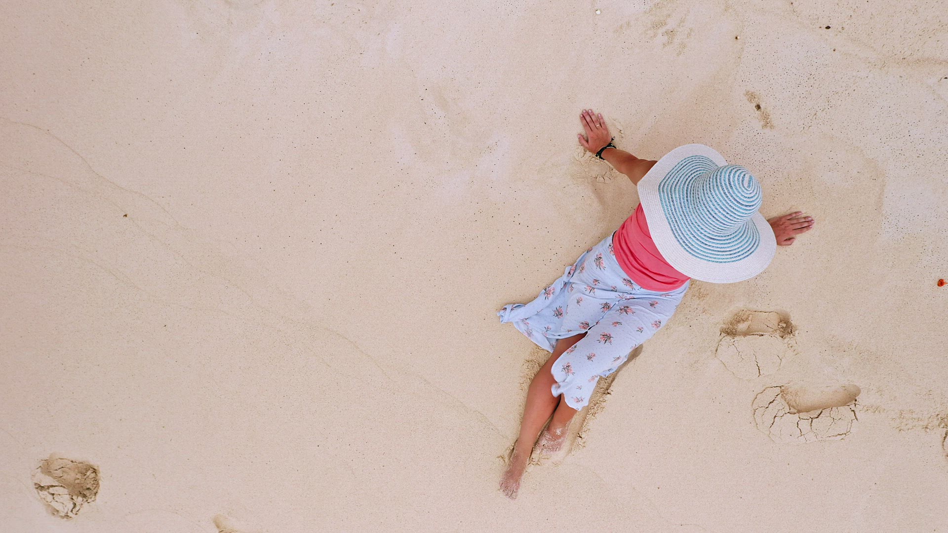 4k aerial view vertical hover up footage. Girl sitting on a white sand beach surrounded by crystal c