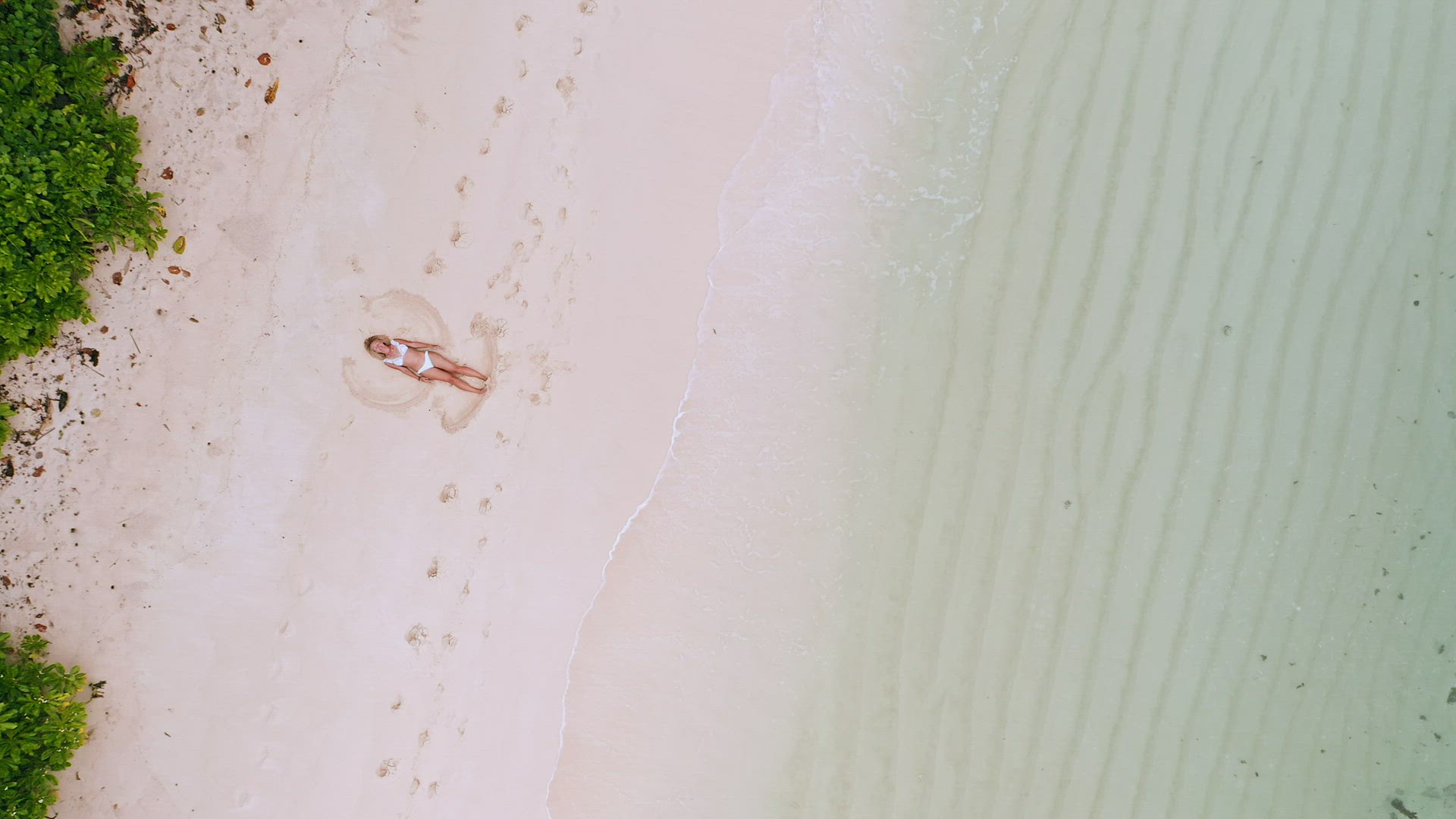 4k aerial vertical move up footage from girl doing sand angel on white tropical beach. Calm ocean wa