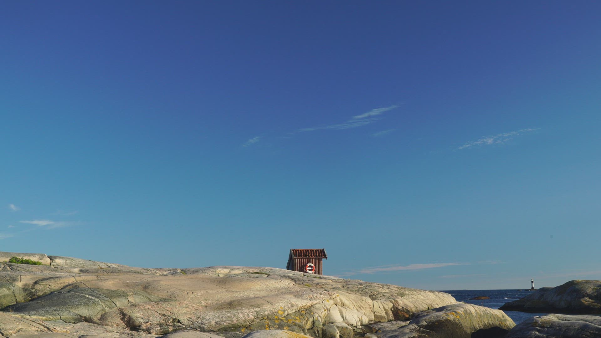view over cliffs in bohuslän - small red house with lifebuoy - lighthouse