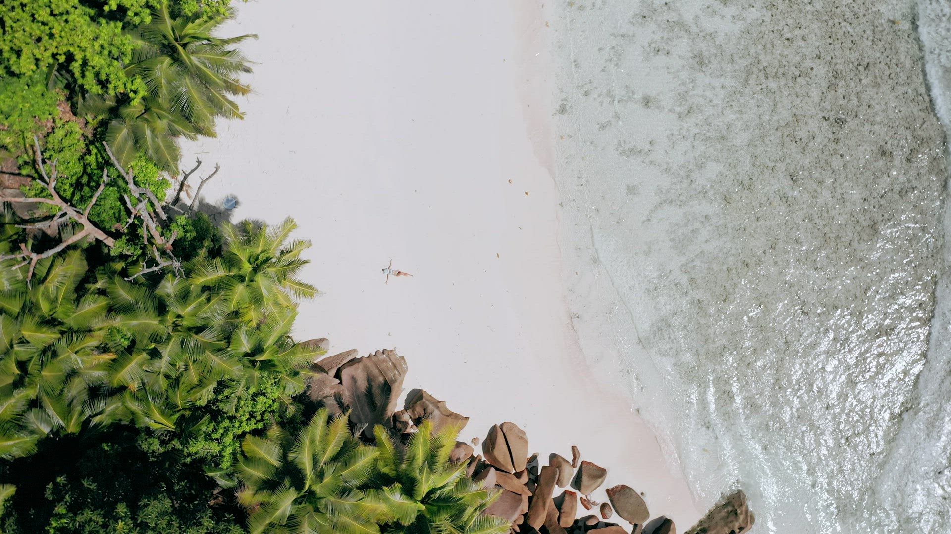 4k aerial view vertical move down footage from girl laying on a white sand beach surrounded by cryst