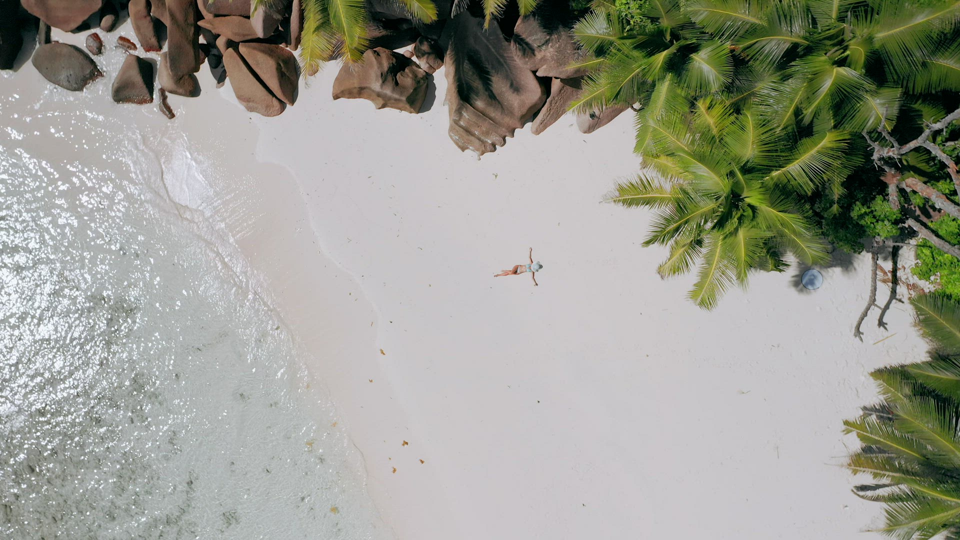 4k aerial view vertical move up footage from girl laying on a white sand beach surrounded by crystal