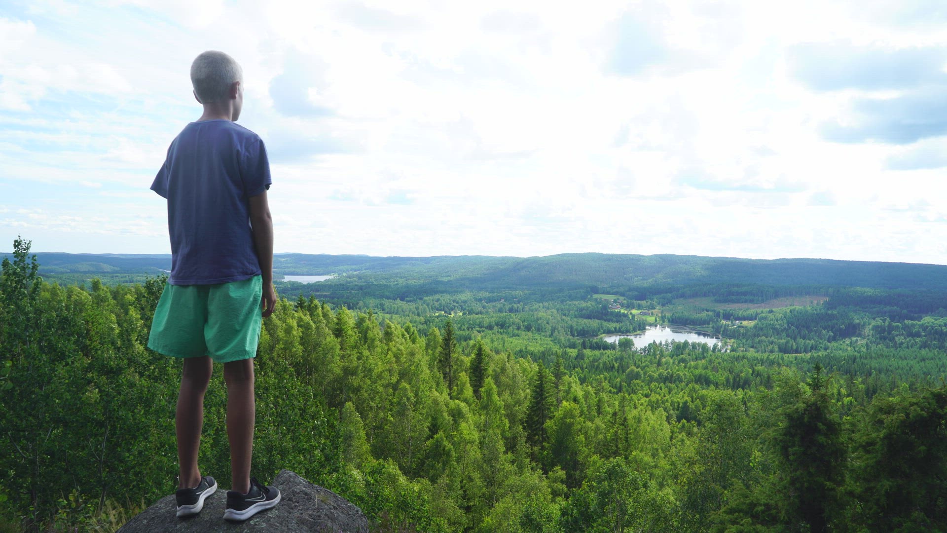 boy standing on mountain - looking out over forest landscape