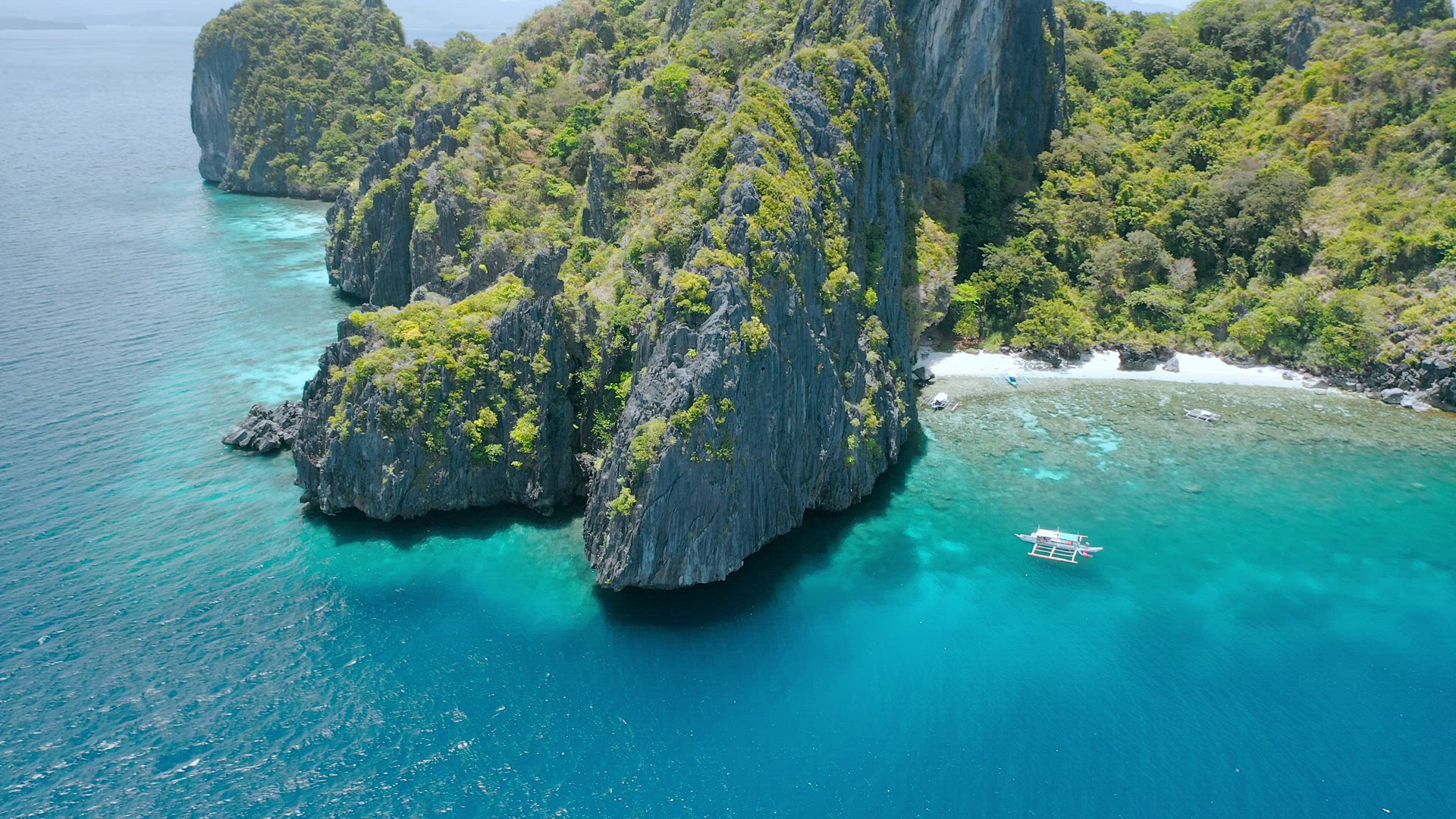 Aerial circle fly above coral reef and banca boats at the beach of limestone rocky Entalula Island, 