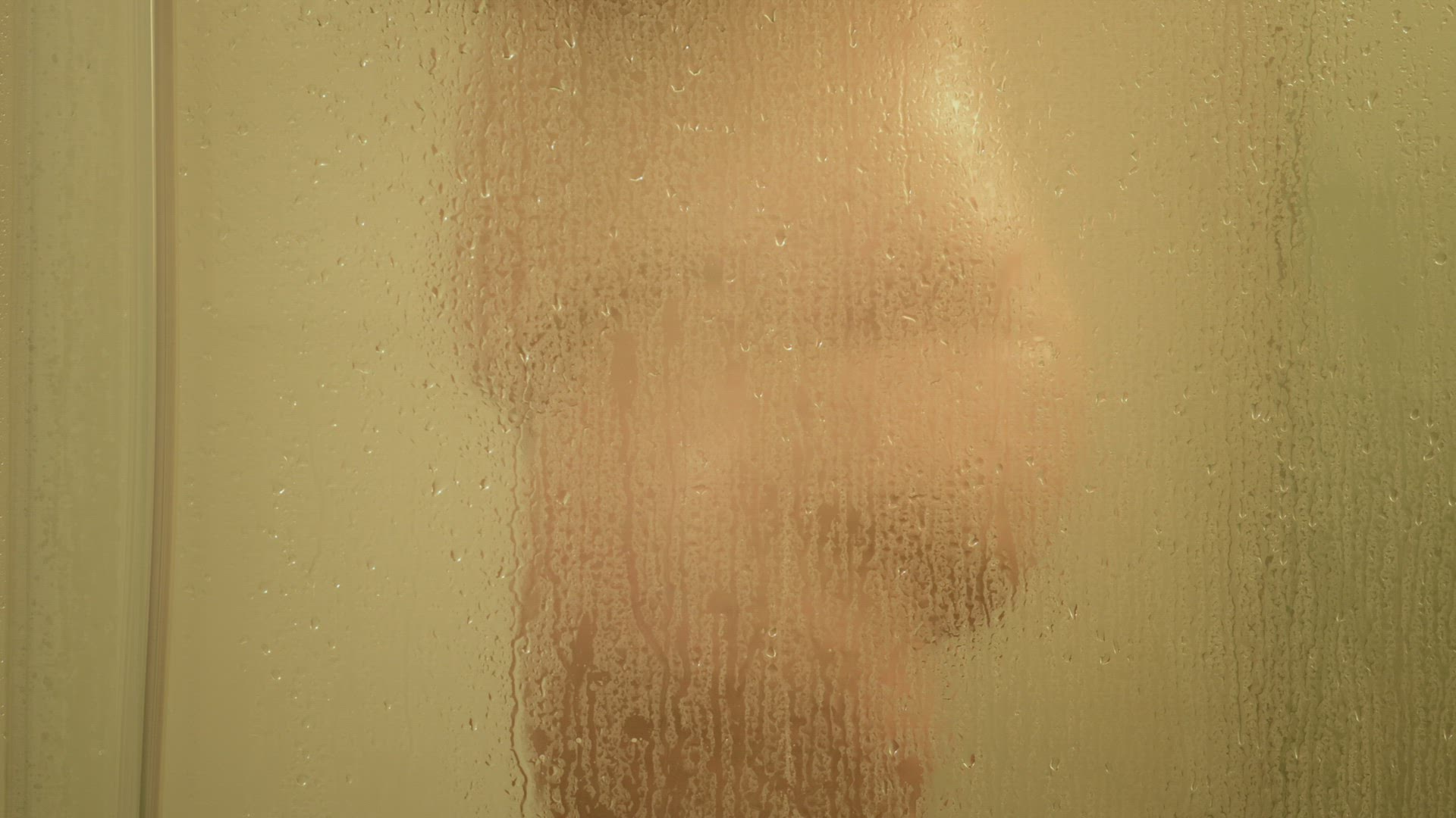 Mid section of woman taking shower, seen through glass
