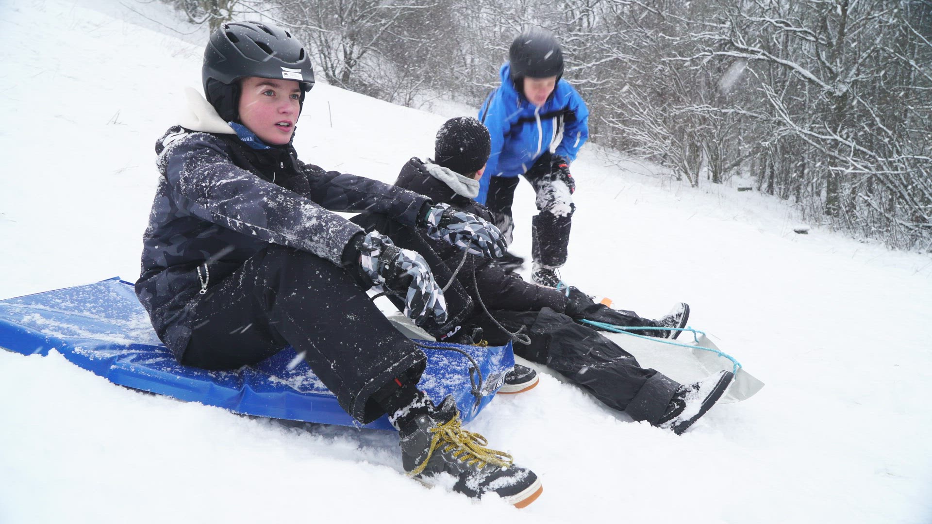 three boys sitting on snow gliders in heavy snowfall
