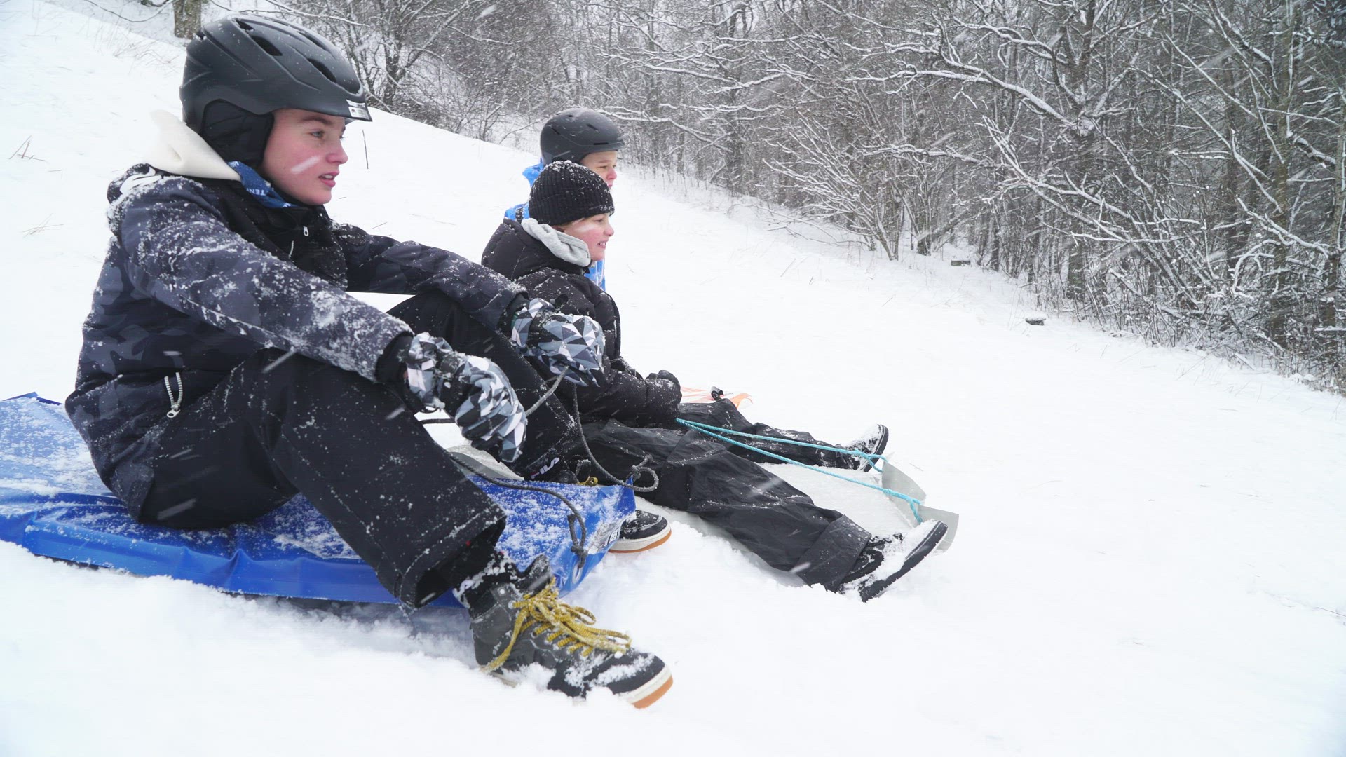 three boys sitting on snow gliders in heavy snowfall