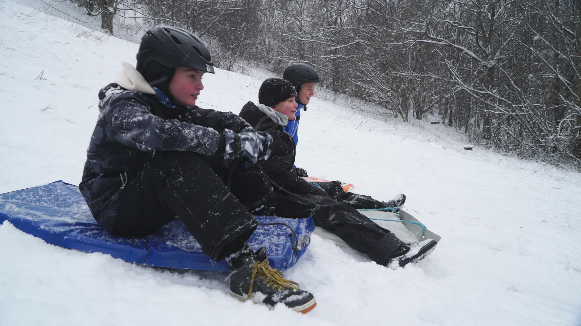 boys on snow gliders - going down steep hill - snowfall
