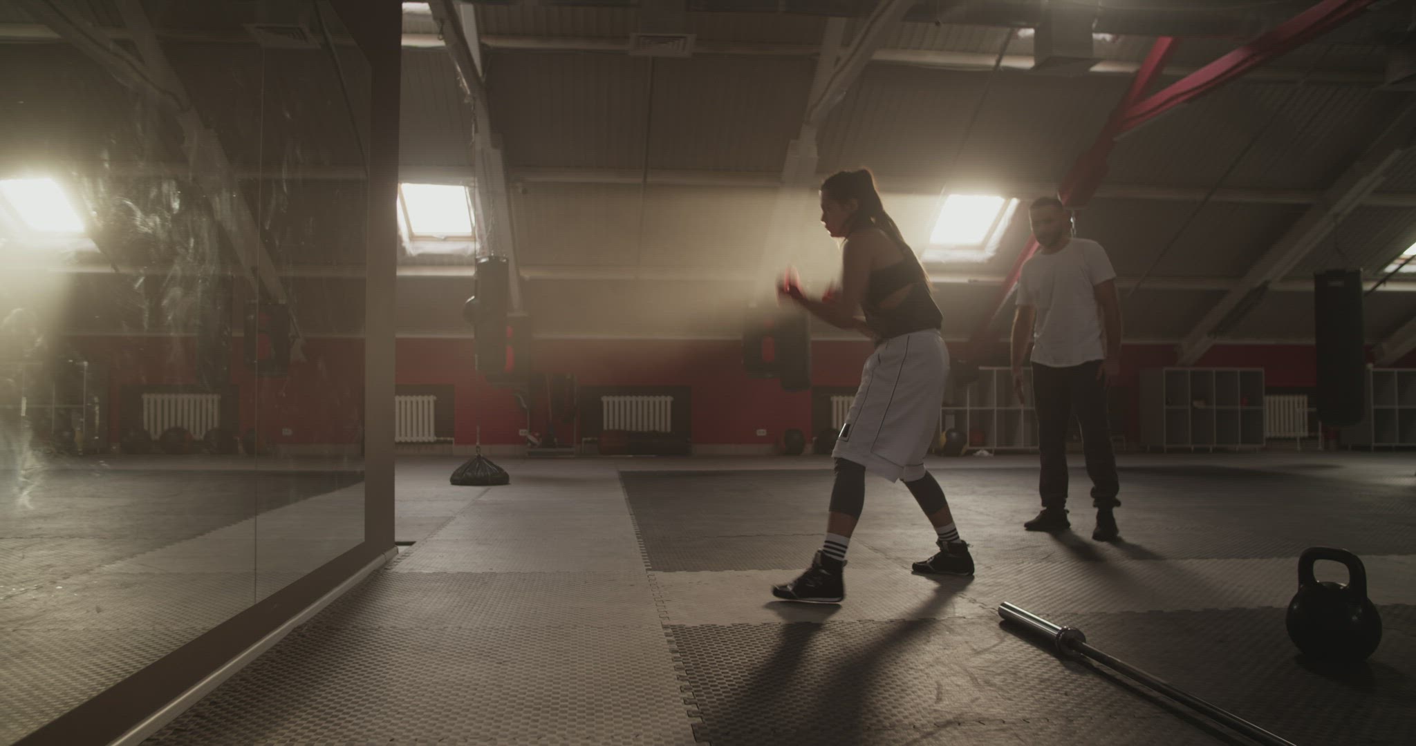 Trainer supporting sportswoman shadow boxing near mirror
