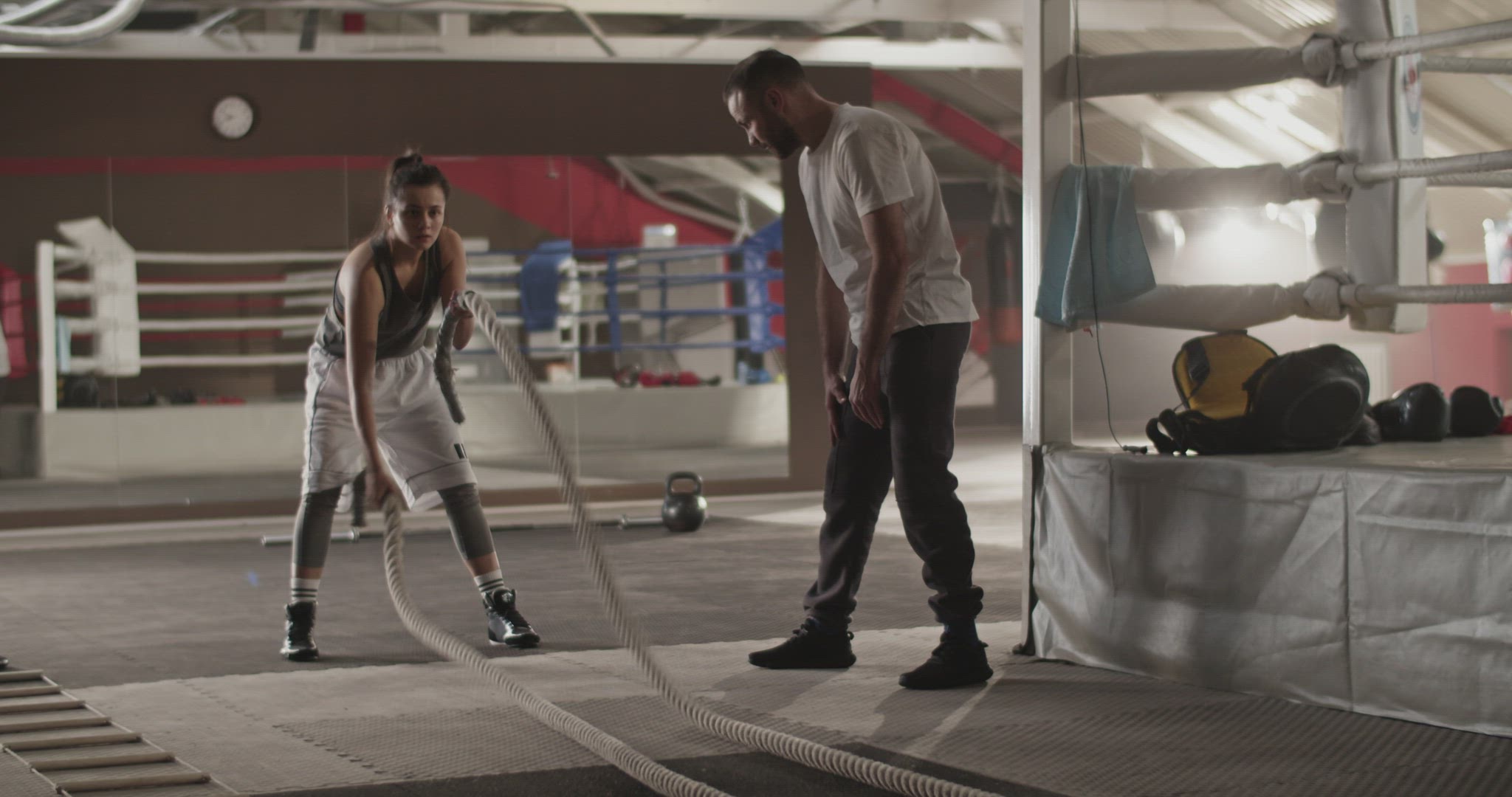 Sportswoman exercising with battle ropes near trainer