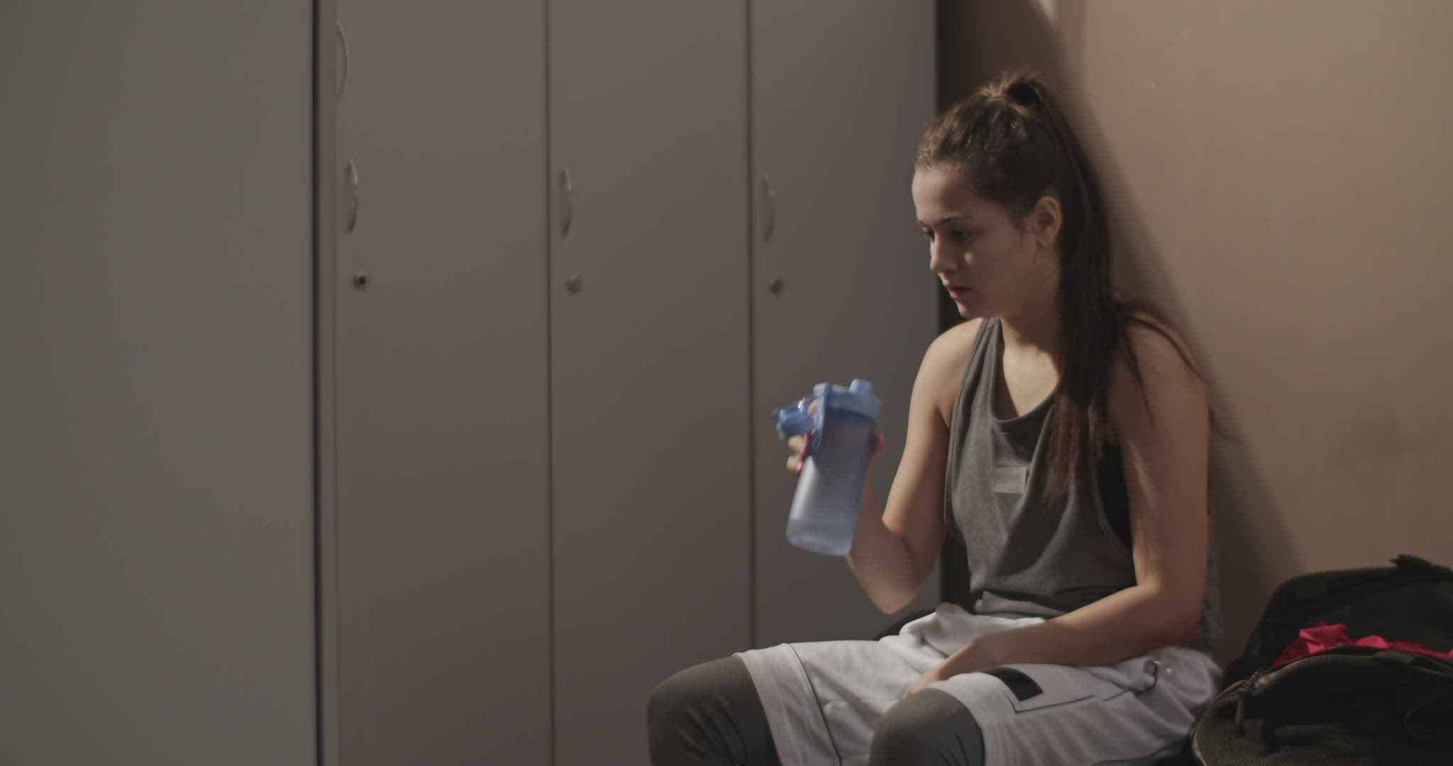 Sportswoman drinking water in dressing room