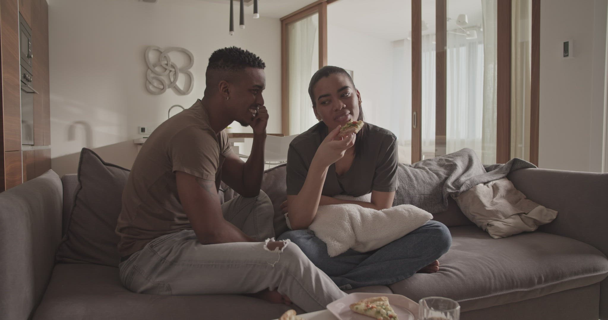Diverse couple eating pizza on sofa