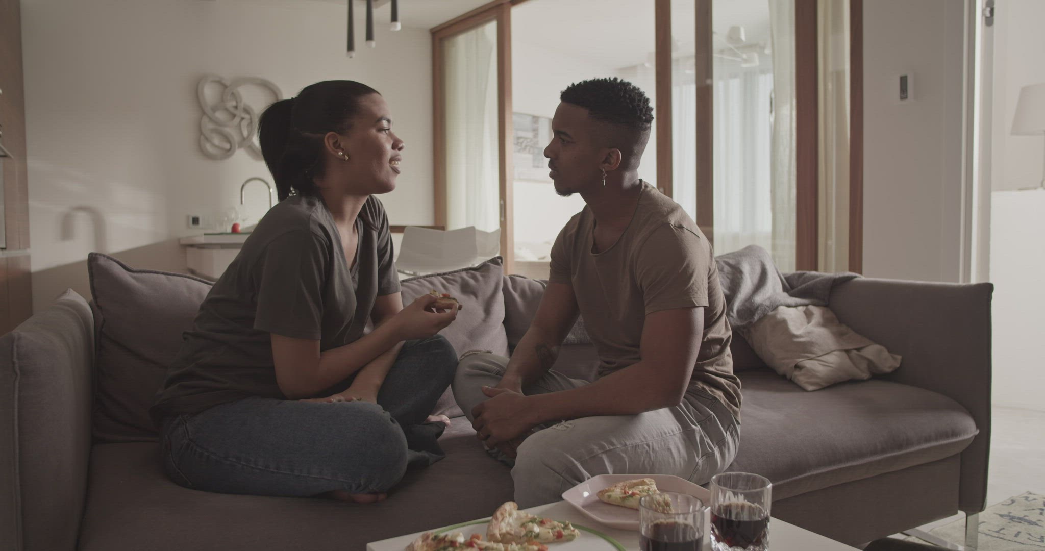 Diverse couple eating pizza on sofa