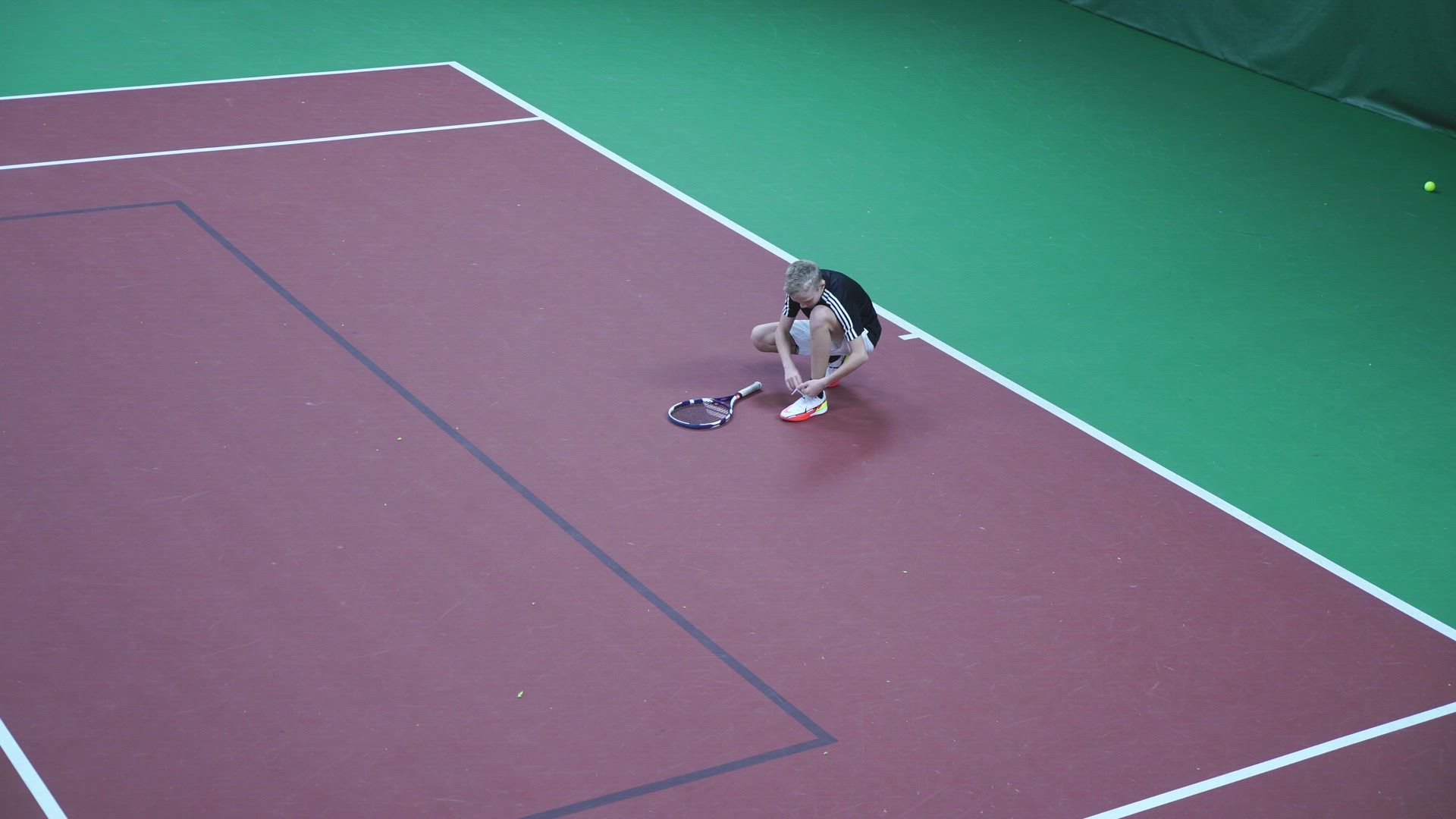 young tennis player at indoor tennis court - sits down and ties his shoelaces
