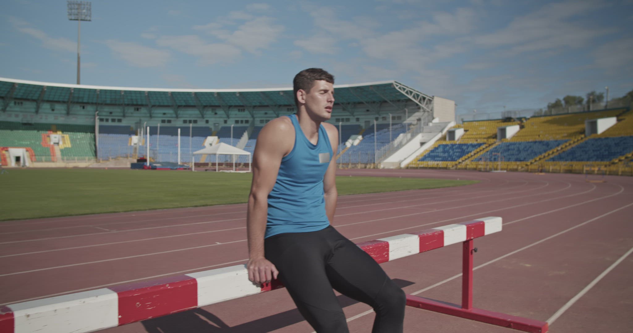 Sweaty sportsman resting near hurdle