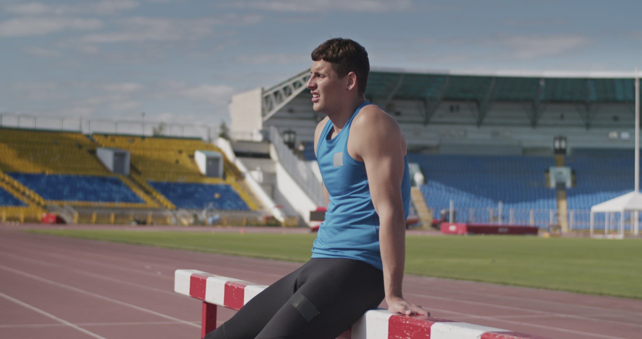 Sweaty sportsman resting near hurdle