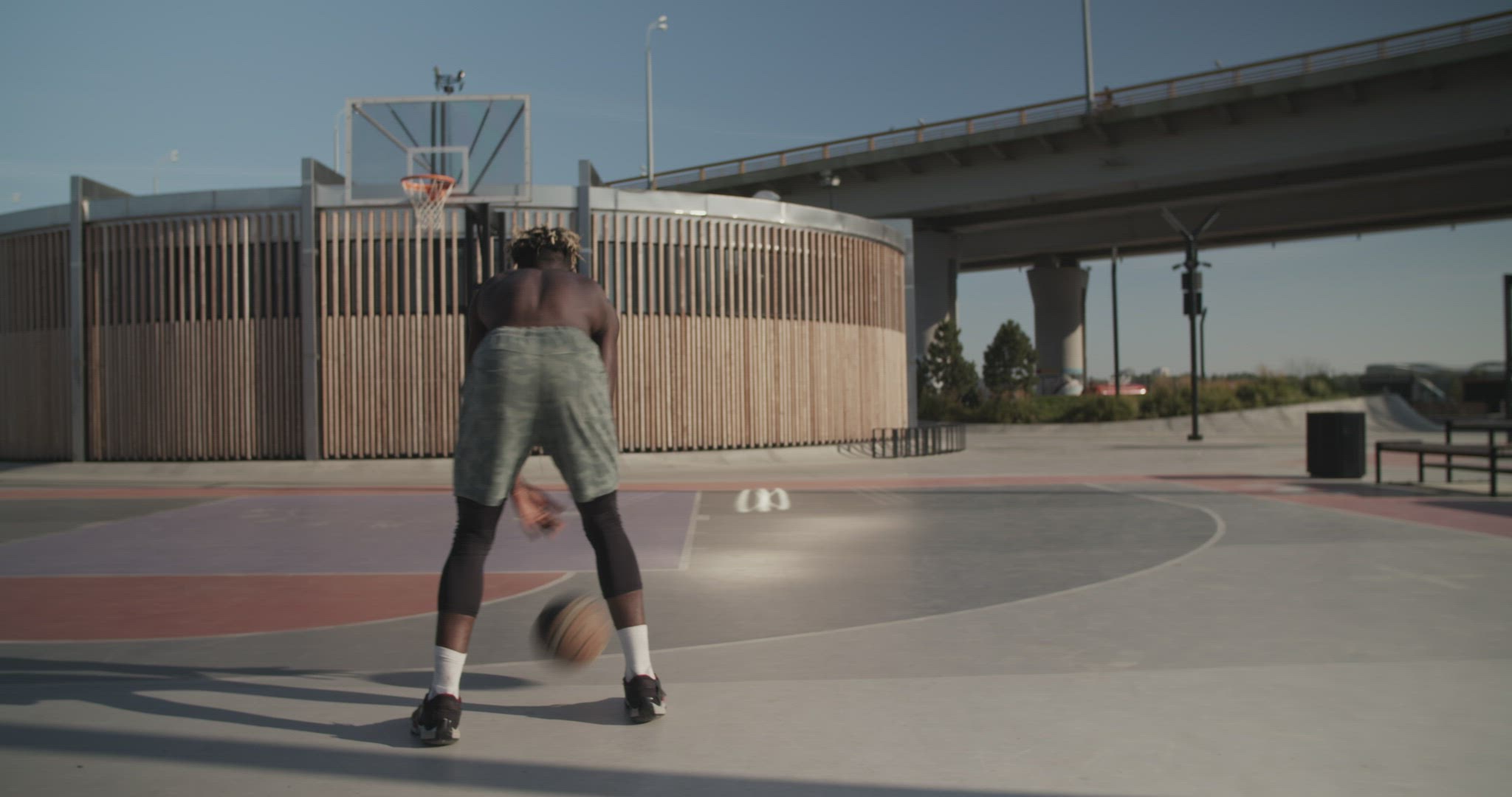 African American sportsman playing basketball near bridge