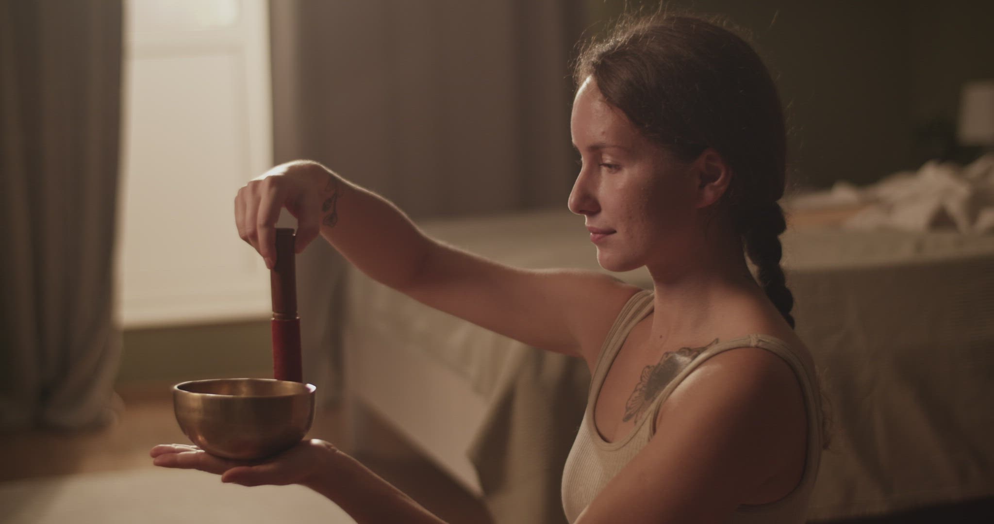 Woman meditating with singing bowl near bed