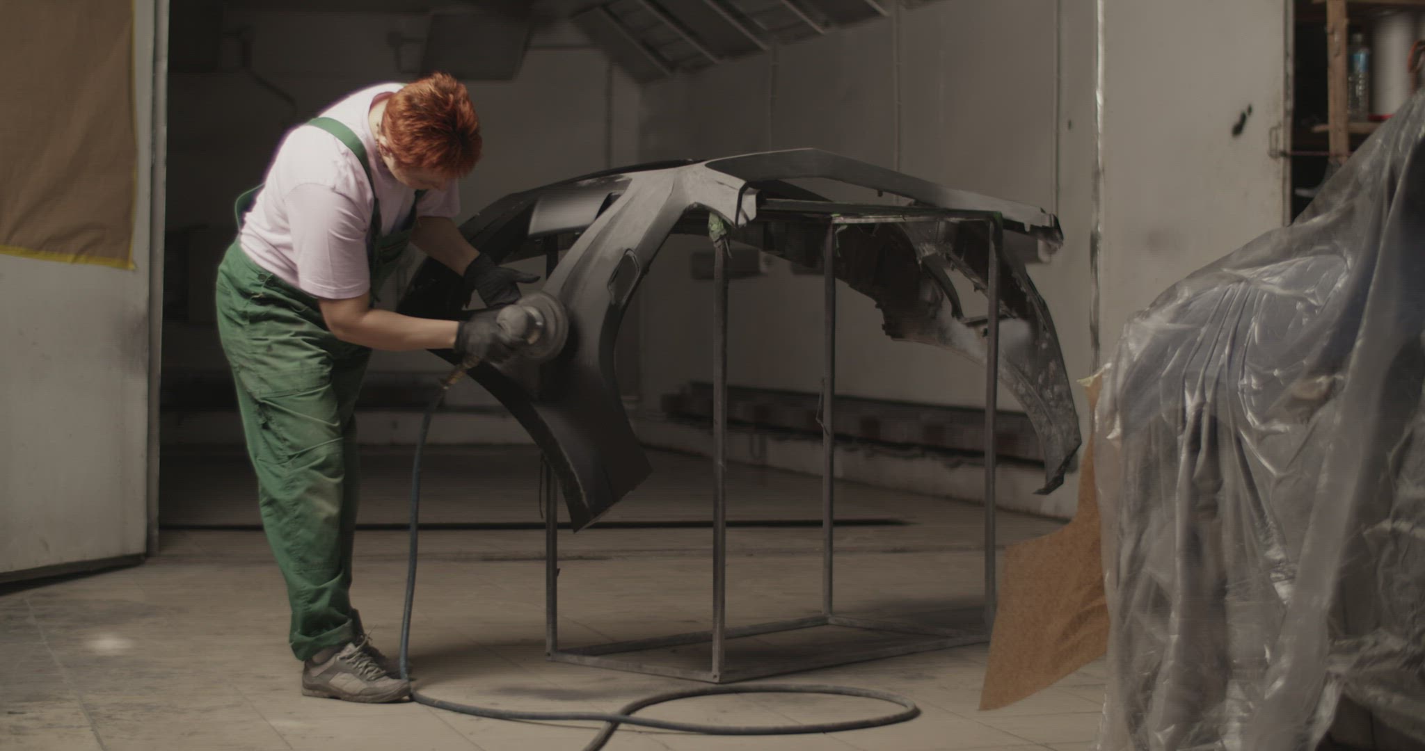 Repairwoman sanding bumper near vehicle