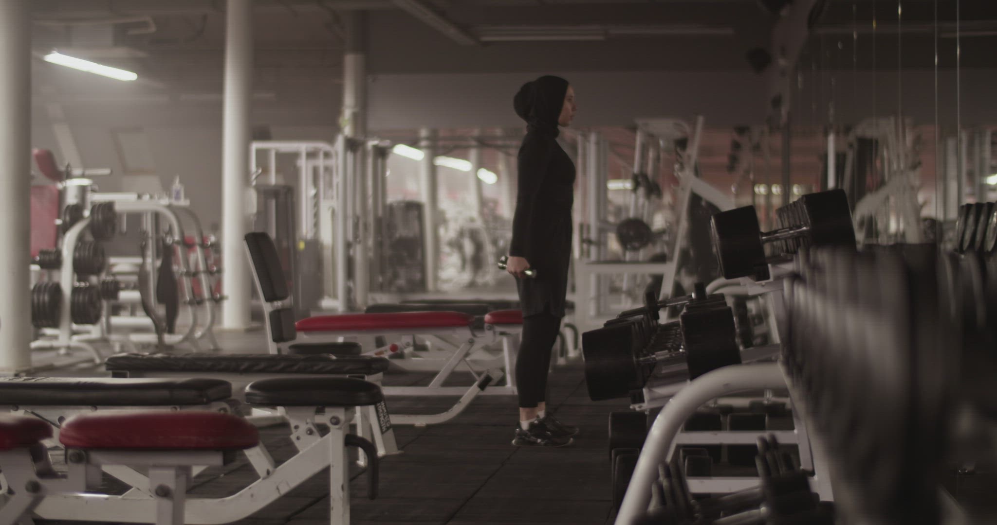 Muslim female athlete doing biceps curls in fitness gym