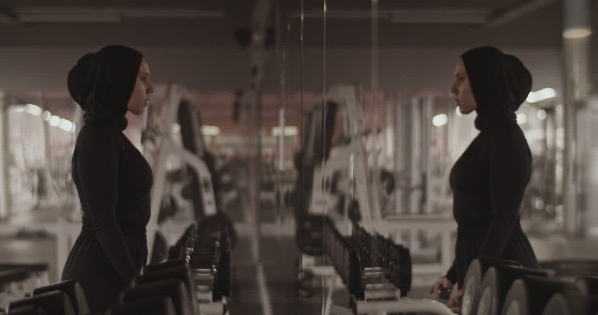 Muslim sportswoman doing biceps curls near mirror