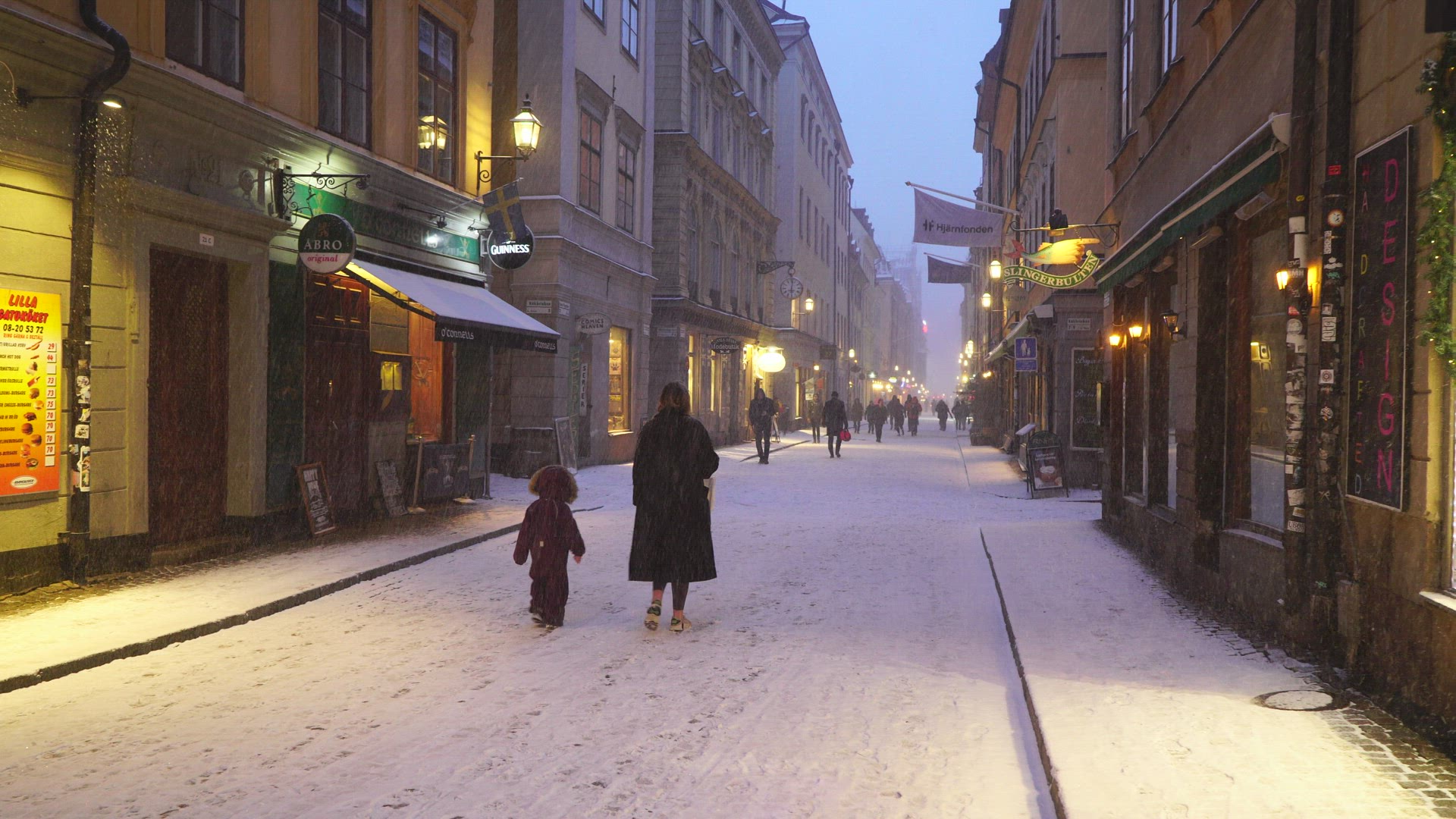 mother and child walking on snowcovered alley in Old Town Stockholm - bicyclist passing
