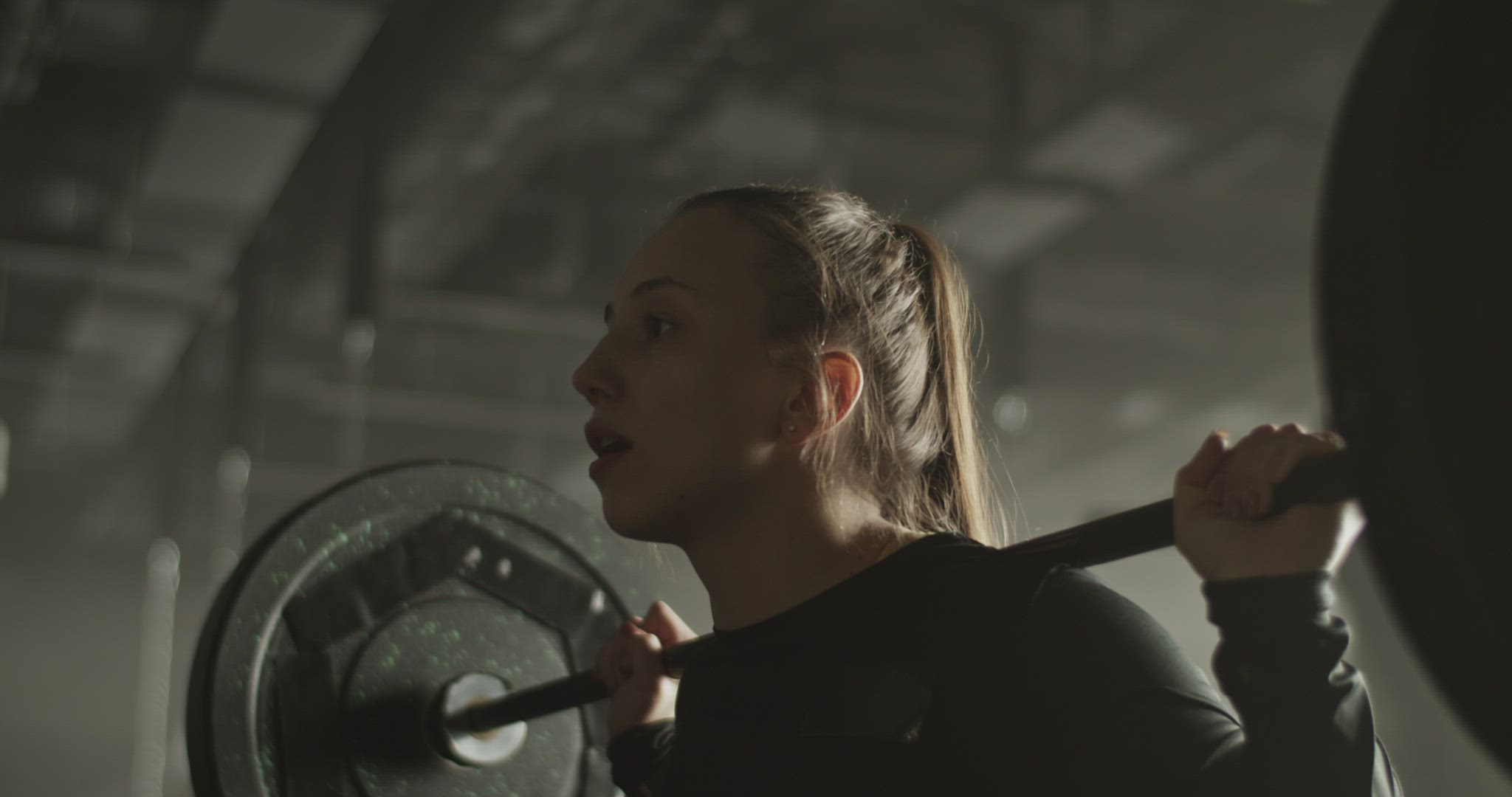 Focused powerful sportswoman squatting with weight in sports club