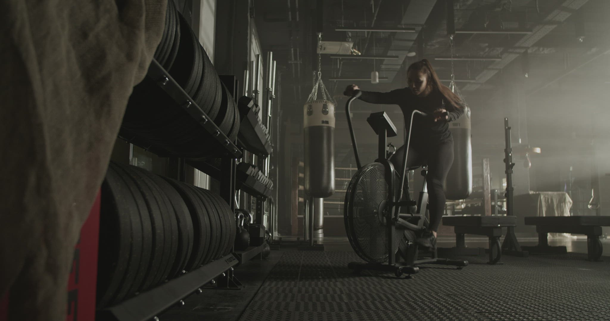 Athletic lady exercising on stationary air bike in gymnasium