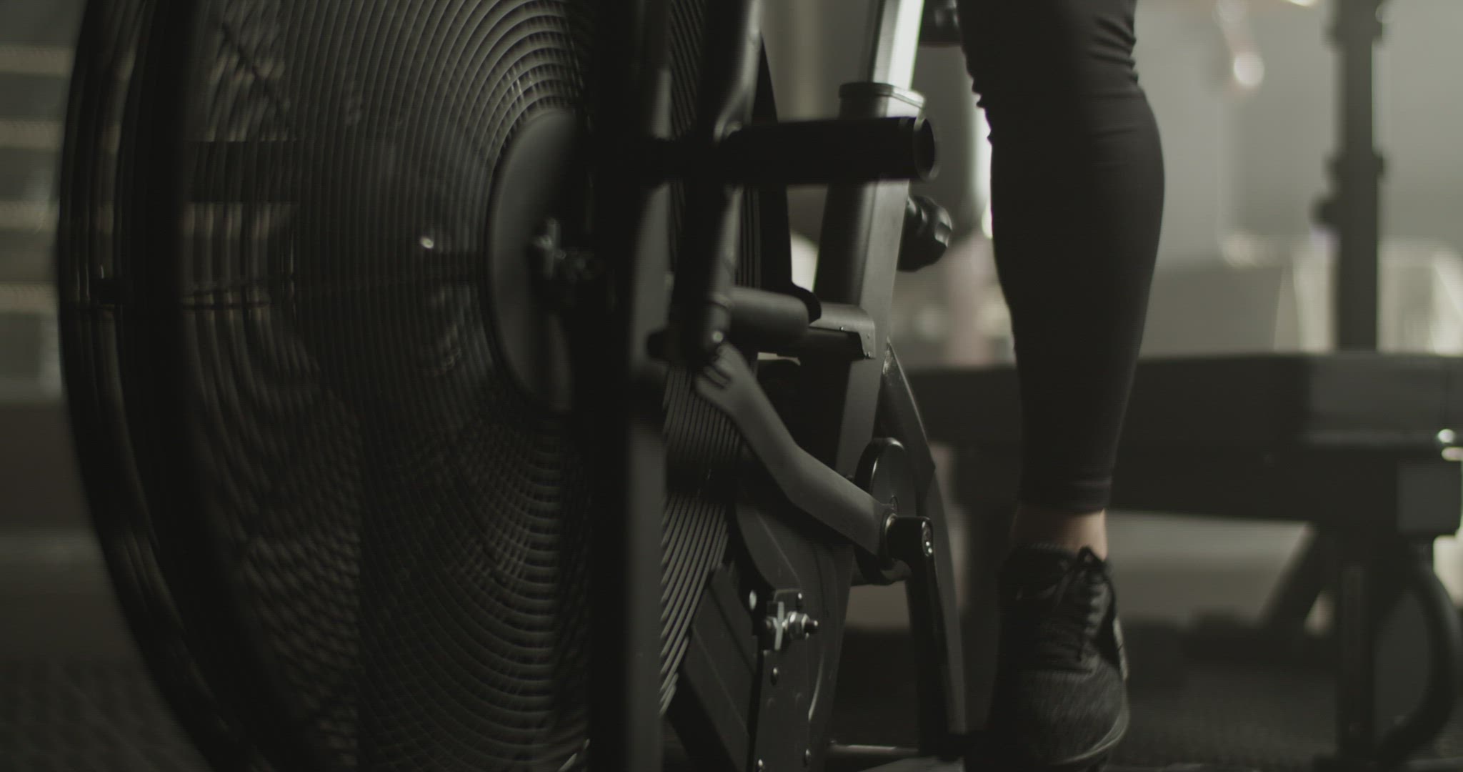 Focused muscular sportswoman exercising on air bike in gym
