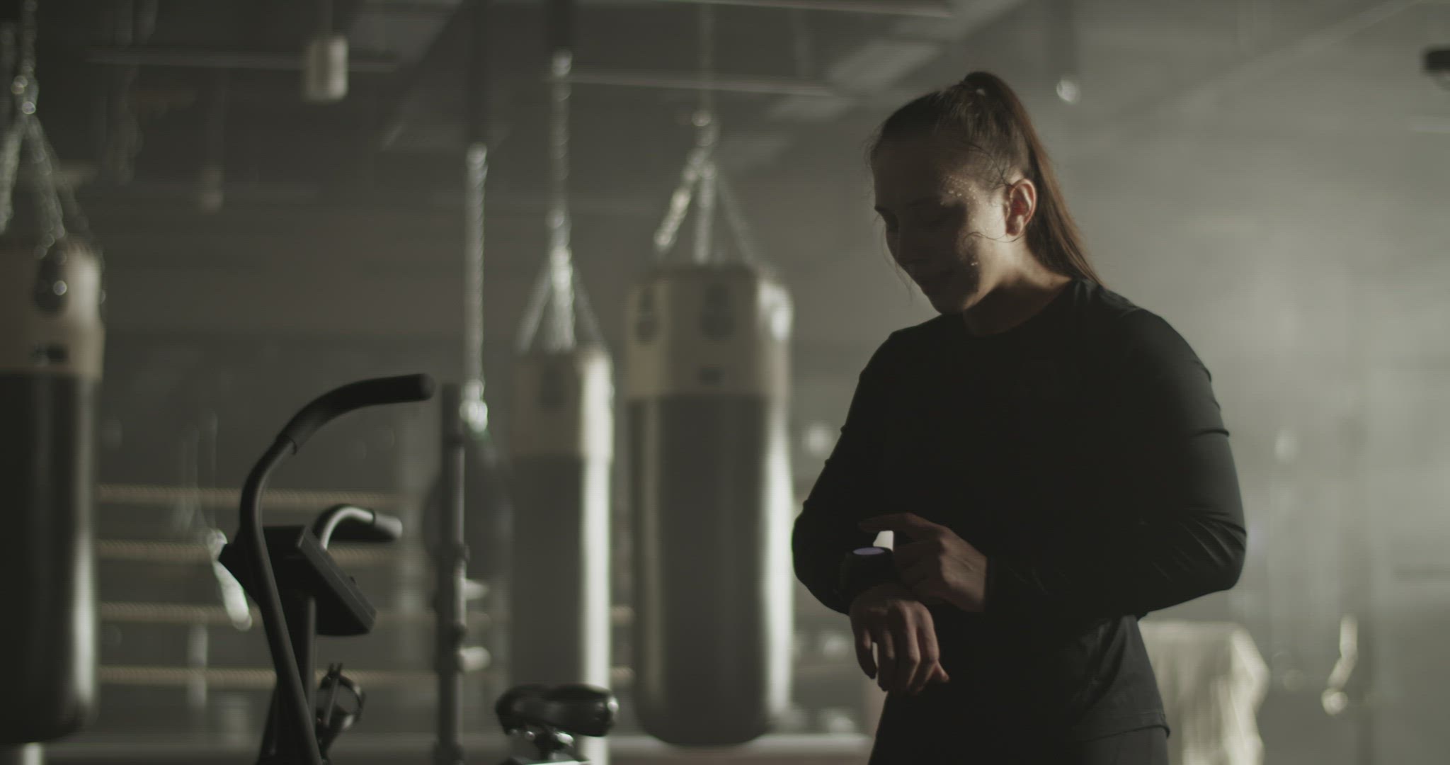 Tired sportive woman checking fitness tracker in gym