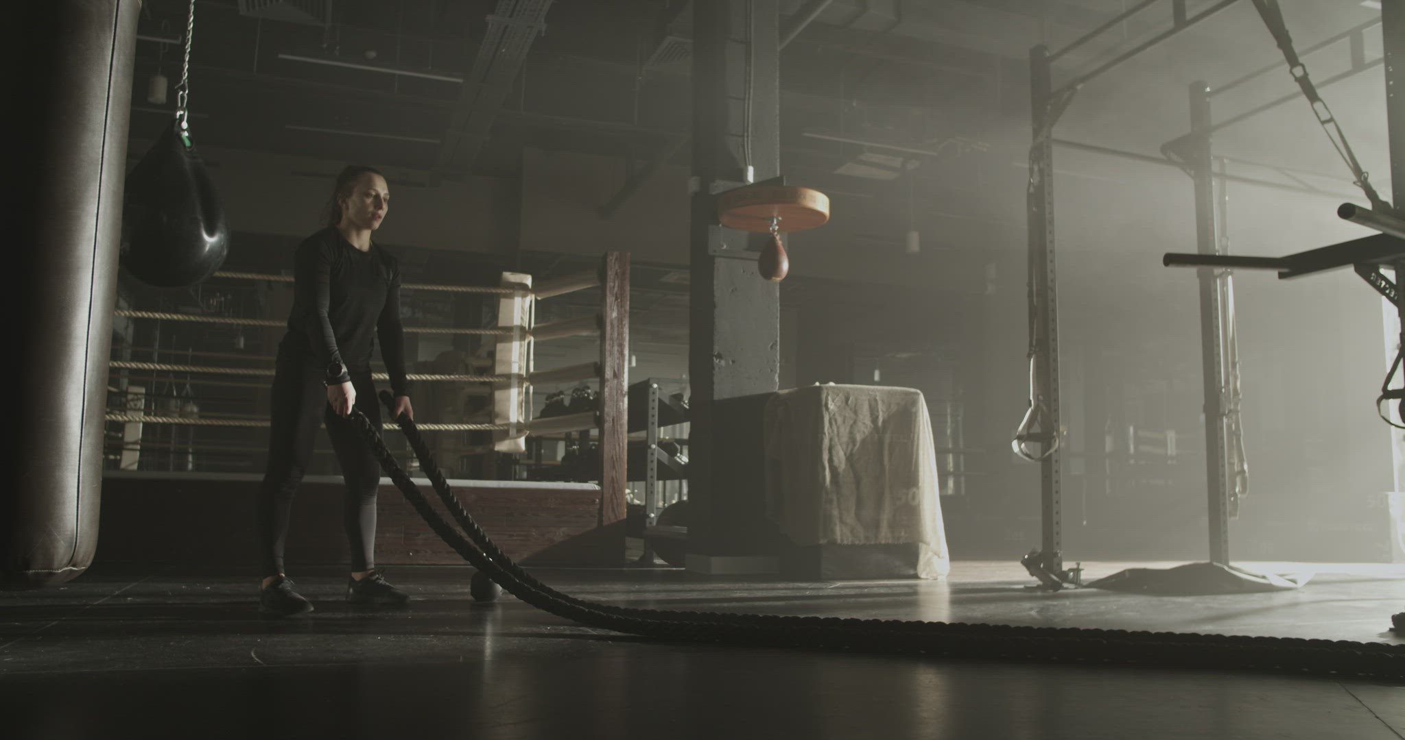 Powerful female athlete exercising with battle ropes in gym
