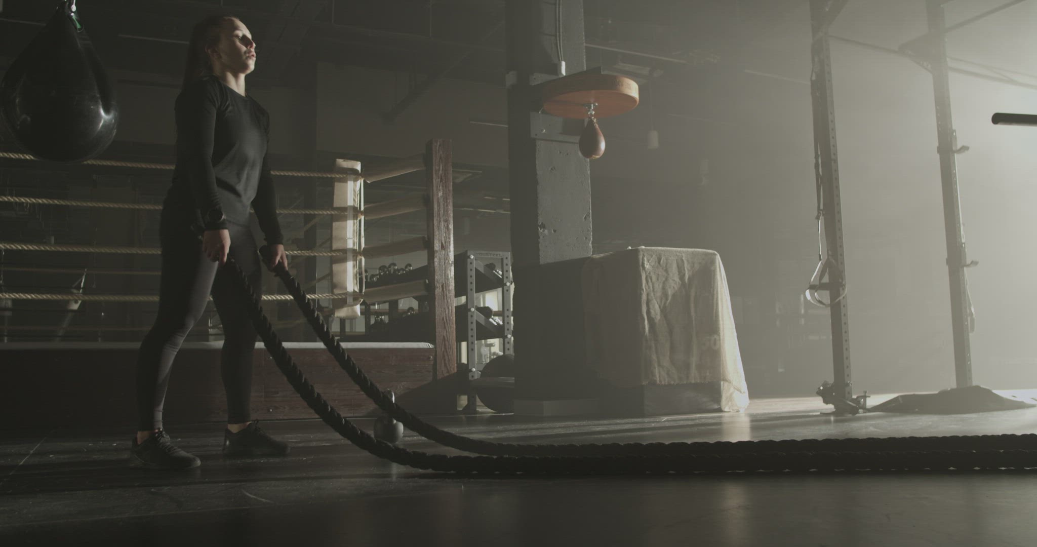 Powerful female athlete exercising with battle ropes in gym