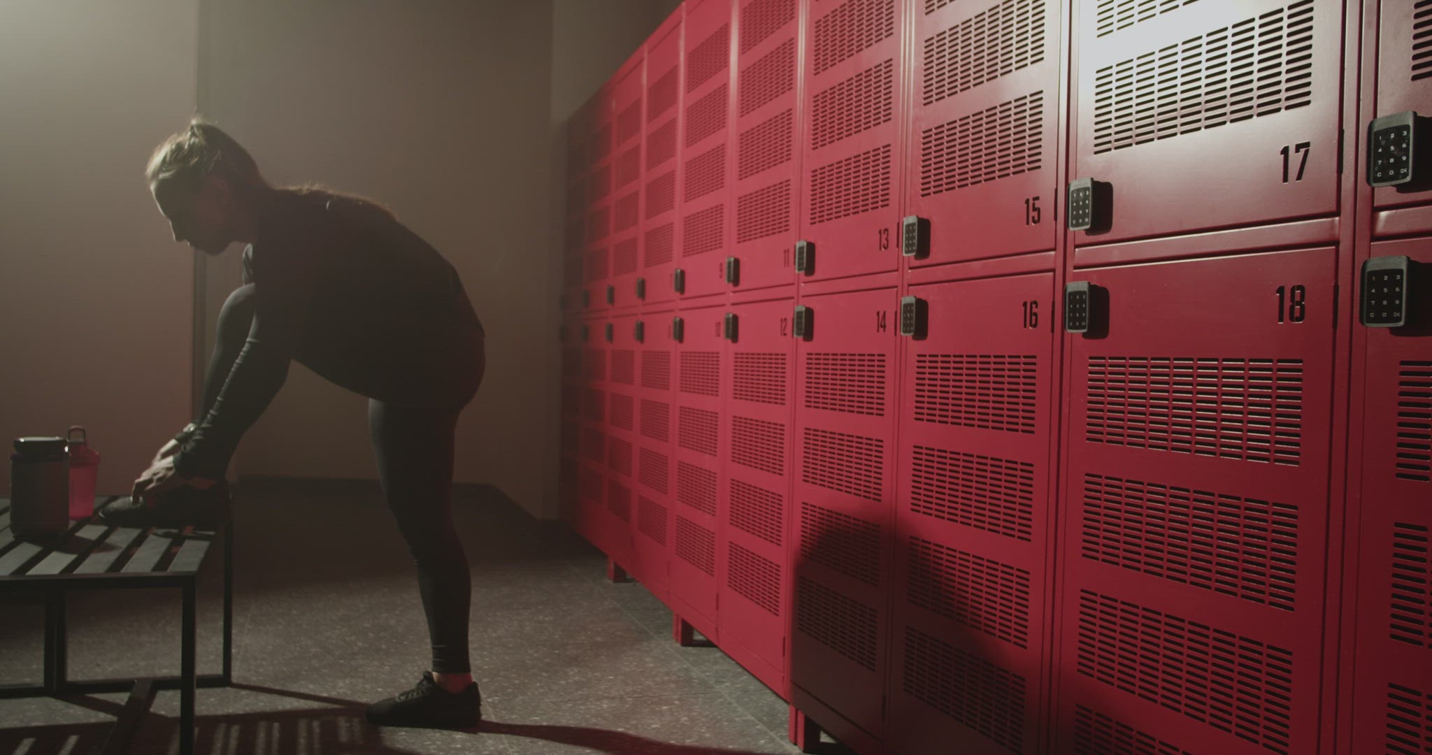 Fit female athlete tying laces on sneakers in locker room