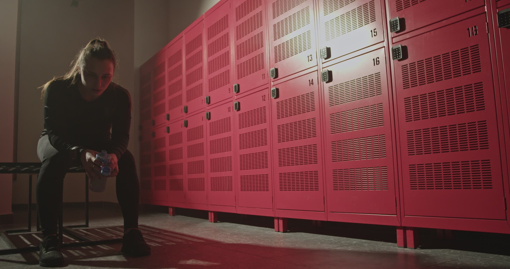 Exhausted female athlete drinking water and resting in locker room