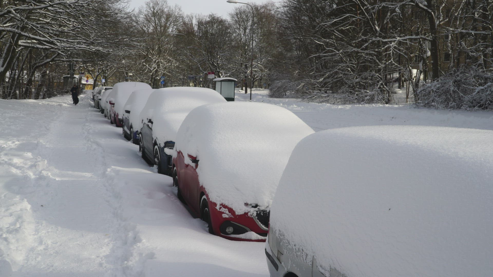 snow covered cars parked on street in Aspudden - stockholm suburb - car passing on street