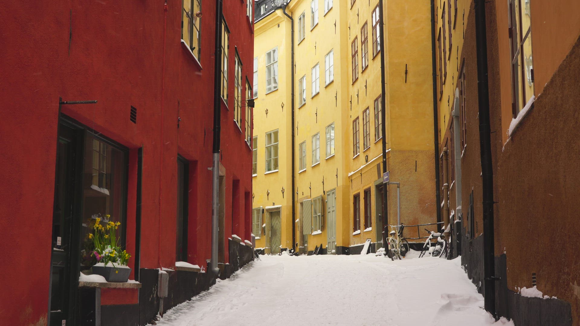 narrow snowy street in old town in stockholm - snow falling on snow covered alley
