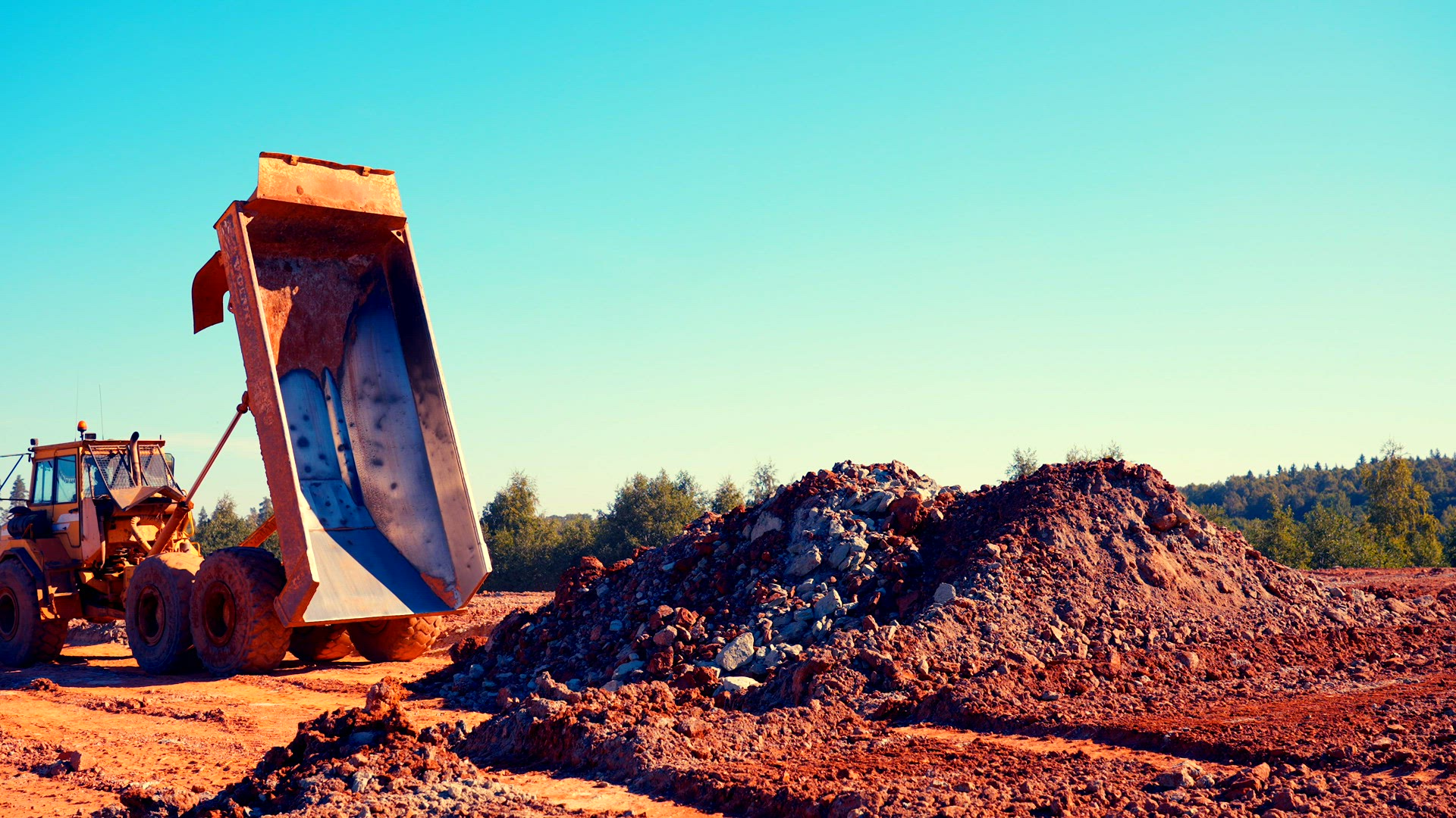 Dump truck dumps red &amp; blue clay in pile.