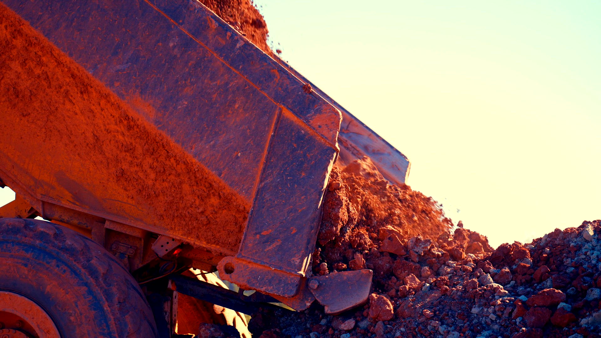 Dump truck dumps red &amp; blue clay in pile.