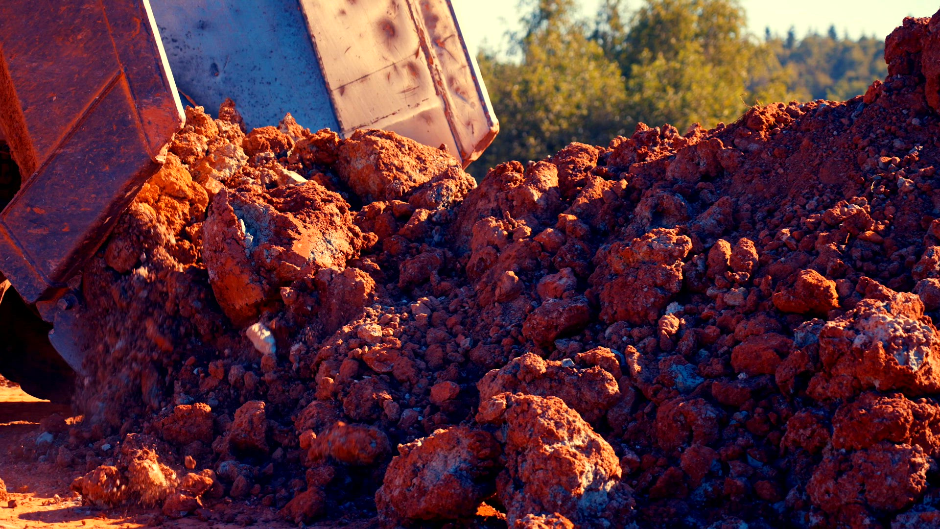 Dump truck dumps red &amp; blue clay in pile.