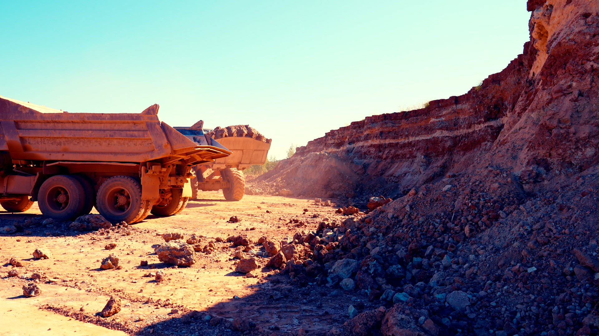 Loader empties its bucket filled with red clay into a dump truck.