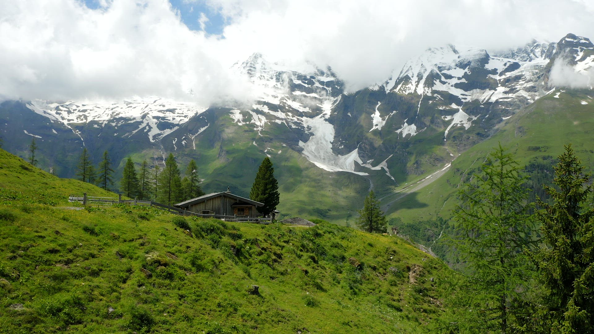 Beautiful old hut and green meadow surrounded by Alps snowy mountains range on summer day landscape 