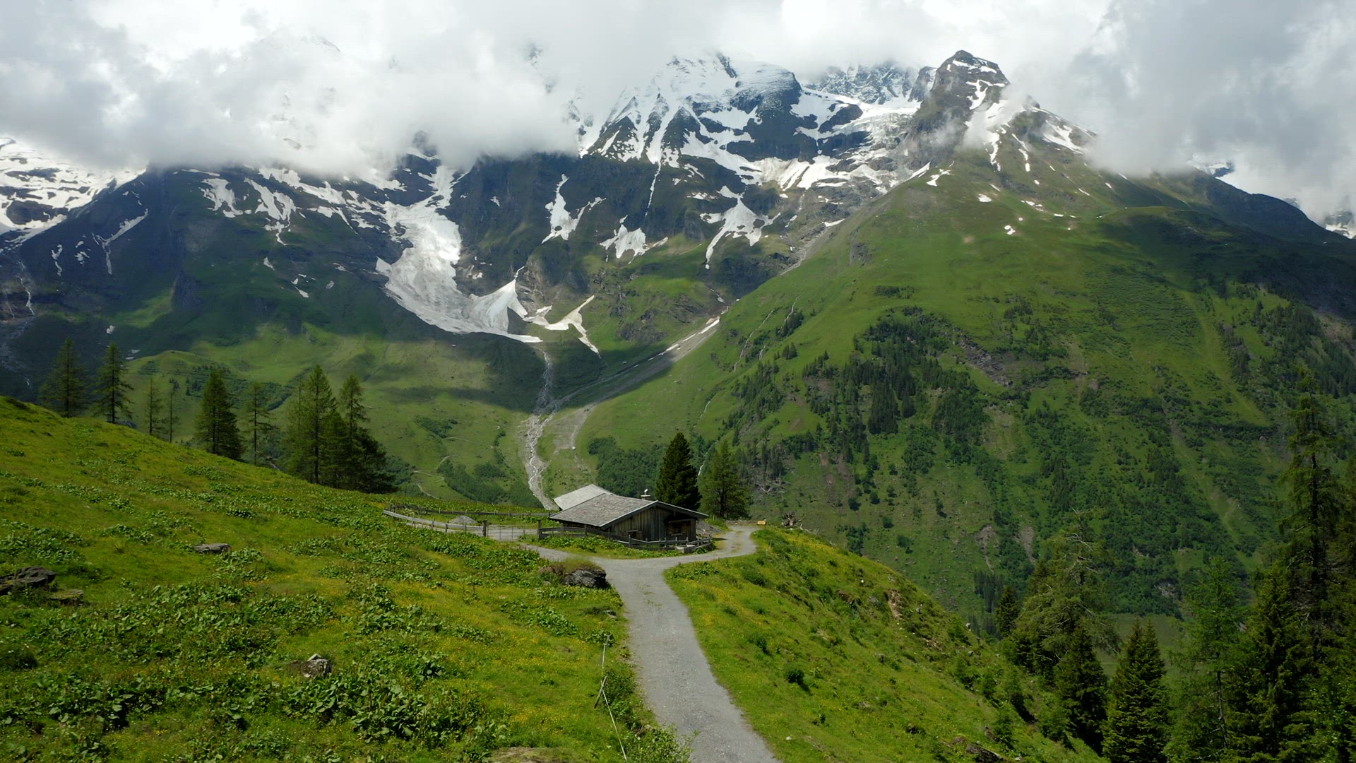 Beautiful old hut and green meadow surrounded by Alps snowy mountains range on summer day landscape 