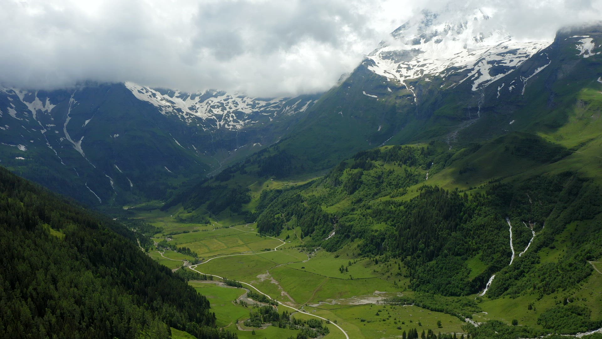 Beautiful scenic green meadow in valley surrounded by Alps snowy mountains range on summer day lands