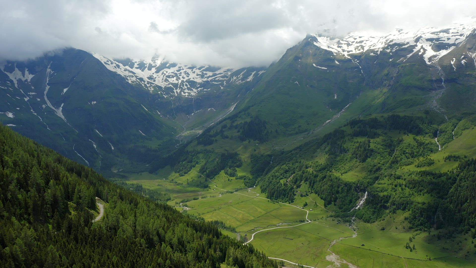 Beautiful scenic green meadow in valley surrounded by Alps snowy mountains range on summer day lands