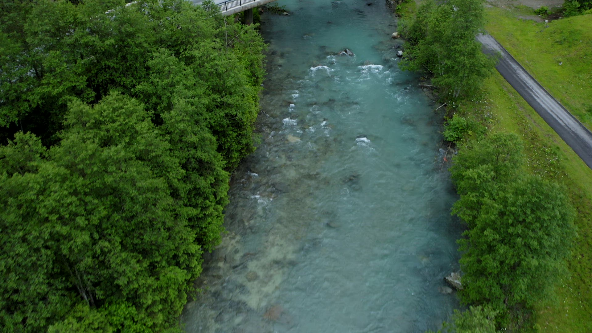Aerial reveal footage of river bridge, blue water steam and waterfall in background. Tirol, Austria
