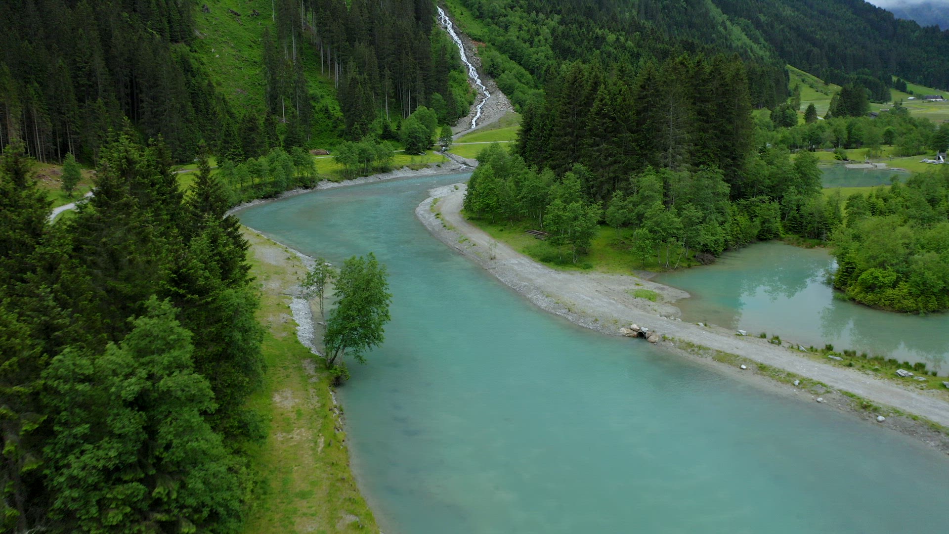 Aerial fly along mountain river with blue water and beautiful waterfall in background. Tirol, Austri