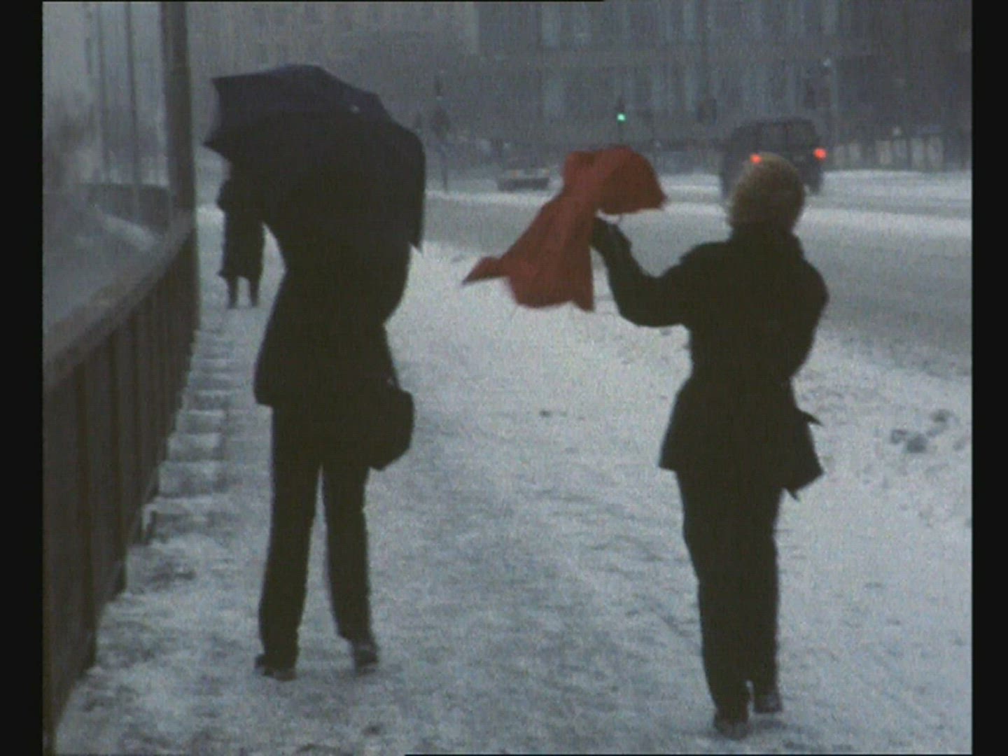 super8mm shot - two woman with umbrellas walking on sidewalk in very strong wind - snow falling
