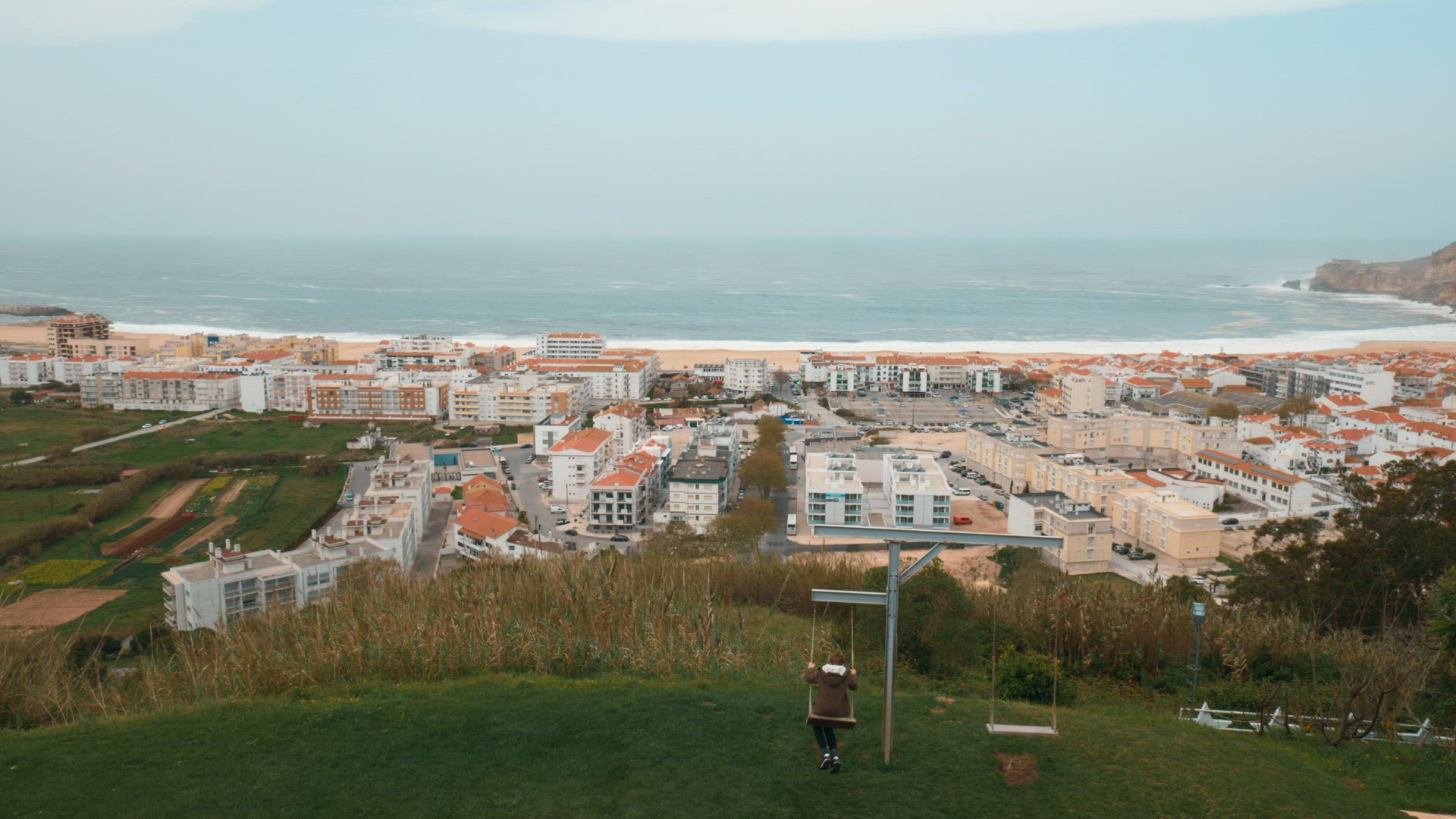 Boy swinging and observing coastal resort town Nazare, Portugal