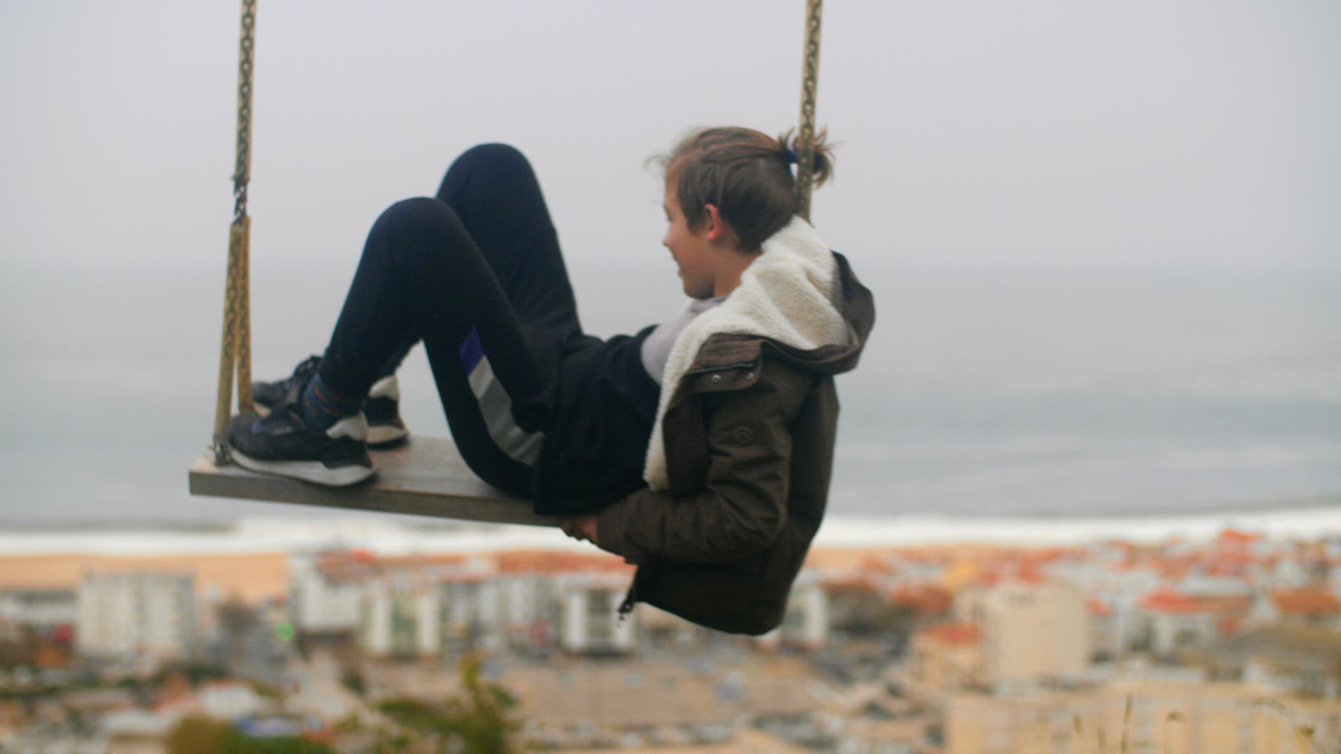 Pensive boy swinging alone against the ocean coast