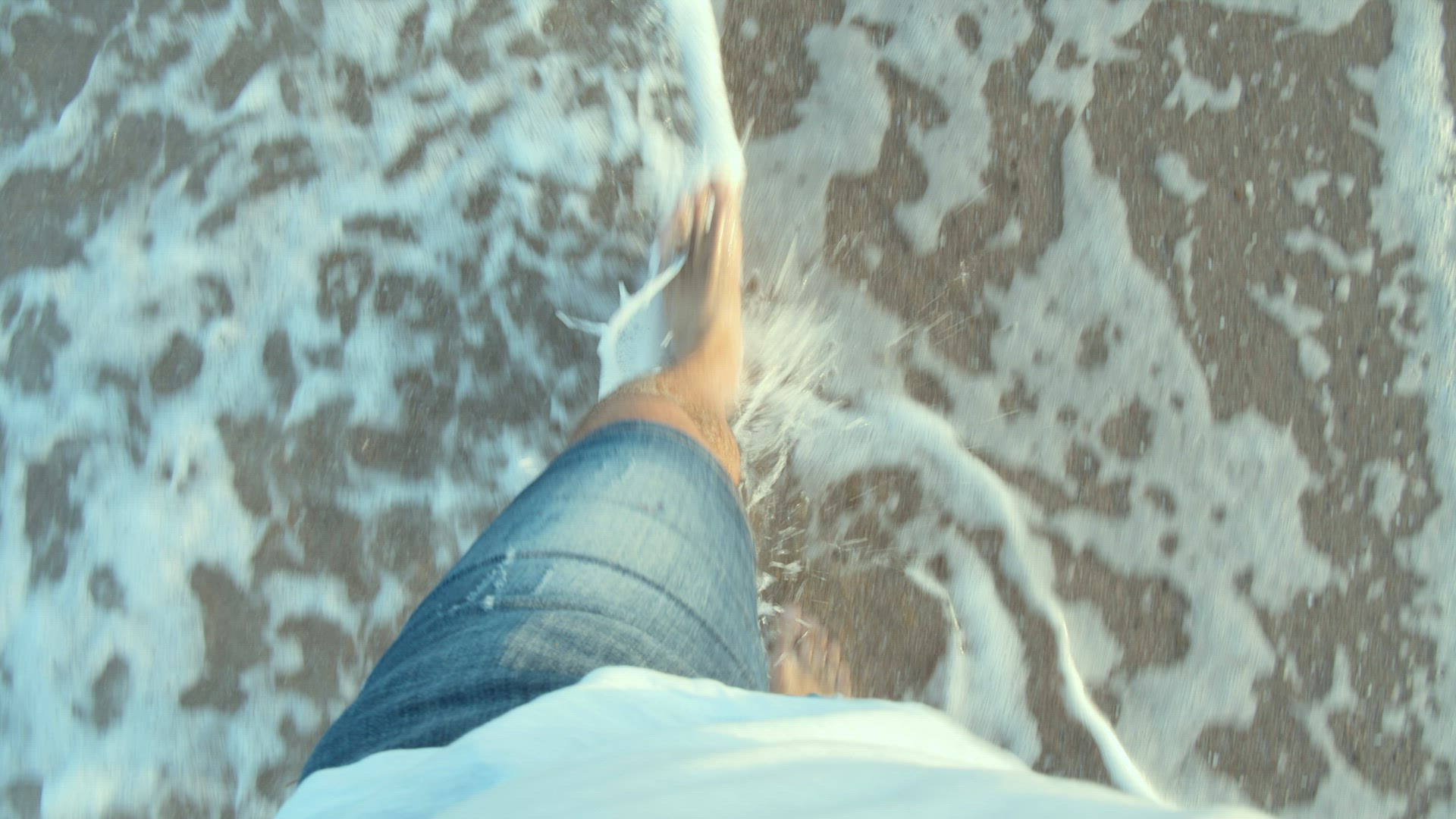 Barefoot man walking on the beach and splashing coastal waves