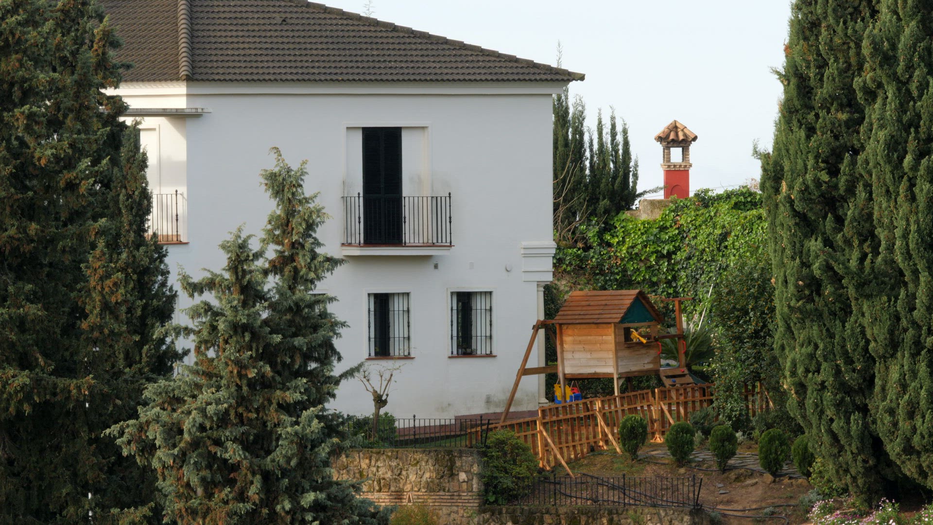 Exterior of two-storey house with kids space and big pine trees aside